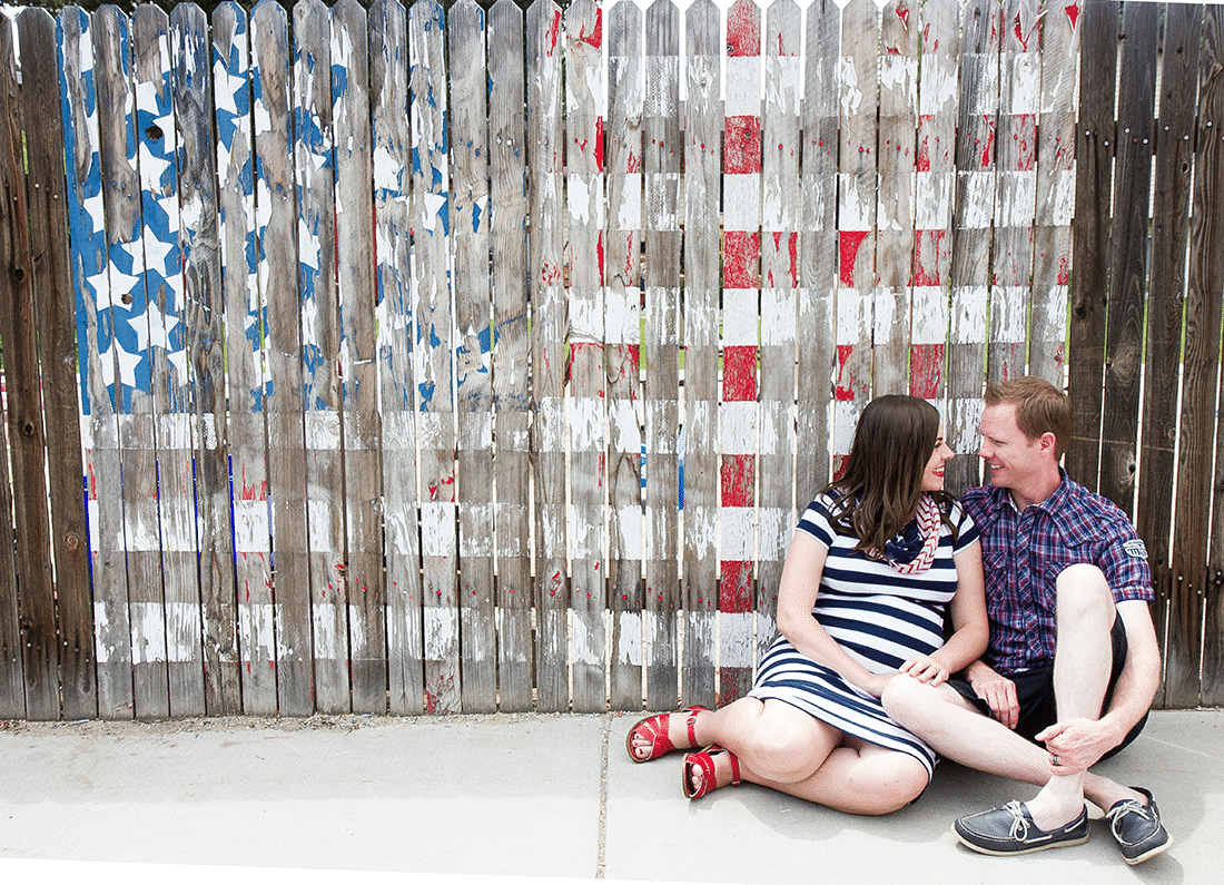 Couple in front of an American flag painted fence. 